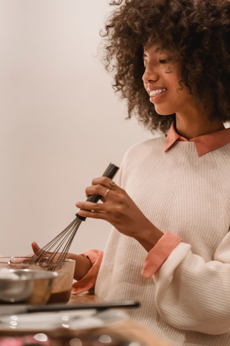 A smiling woman mixing batter with a whisk in her kitchen.