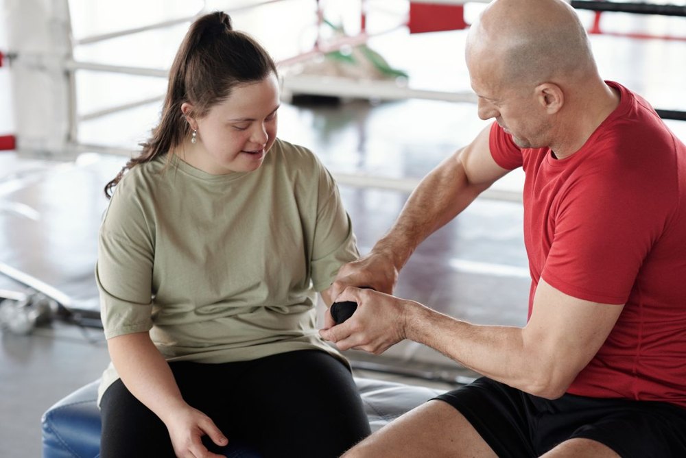 An adult woman taking part in a fitness activity with a trainer providing individual support.