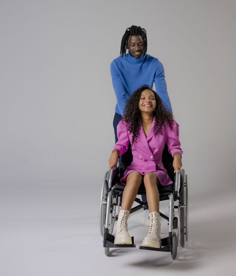 A smiling man assisting a woman who uses a wheelchair.